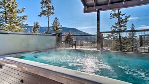 Ein Whirlpool mit Holzterrasse, umgeben von Bäumen und Blick auf die Berge.