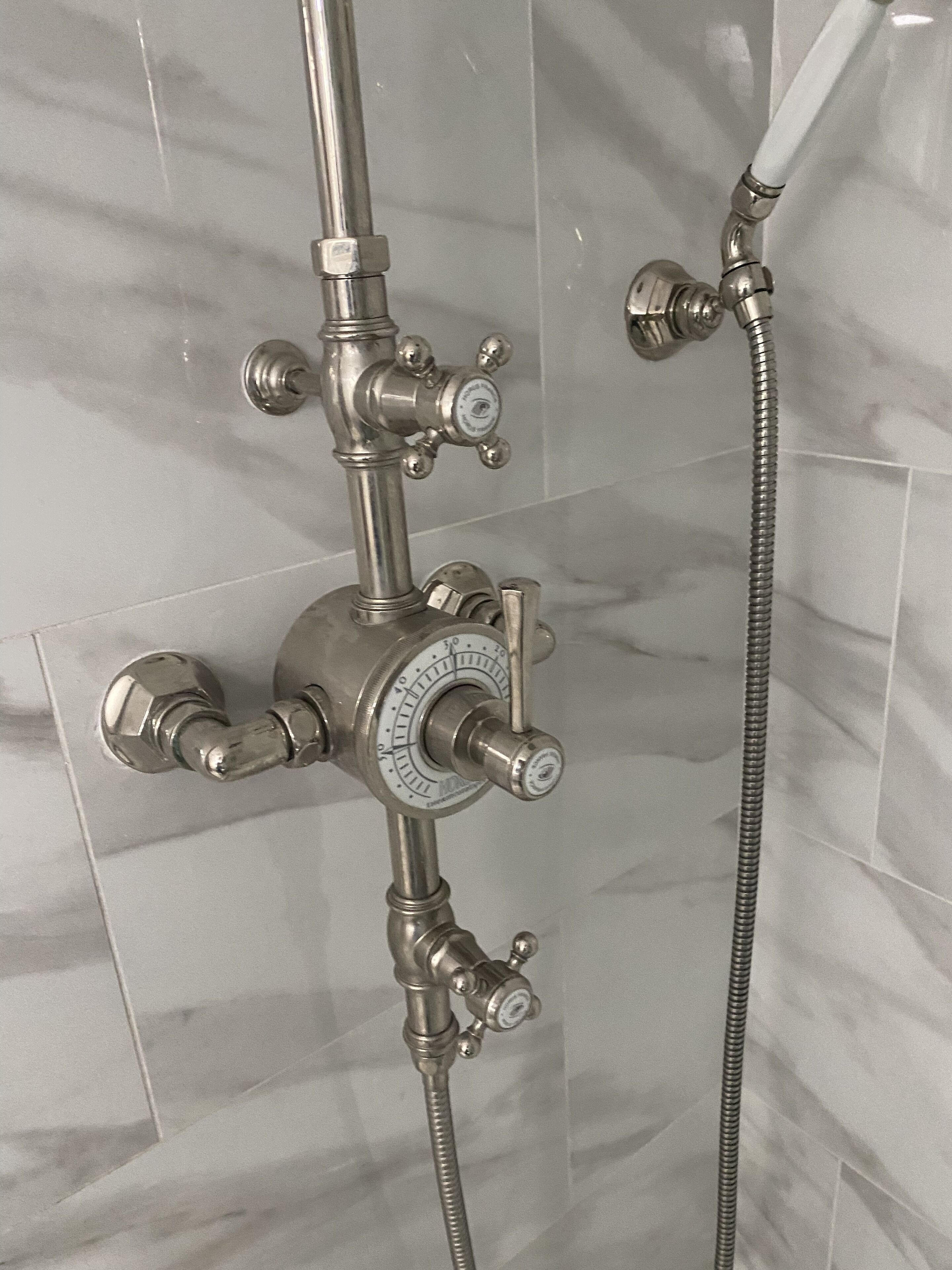 A bathroom with a shower system, including a control knob and a handheld showerhead.