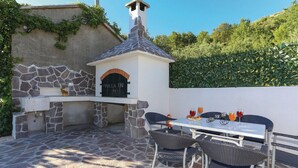 Une cuisine extérieure avec des murs en pierre, une cheminée et une table avec des chaises.