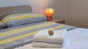 Un lit bien fait, avec une couette blanche, un objet décoratif en bois et une lampe sur une table de chevet.