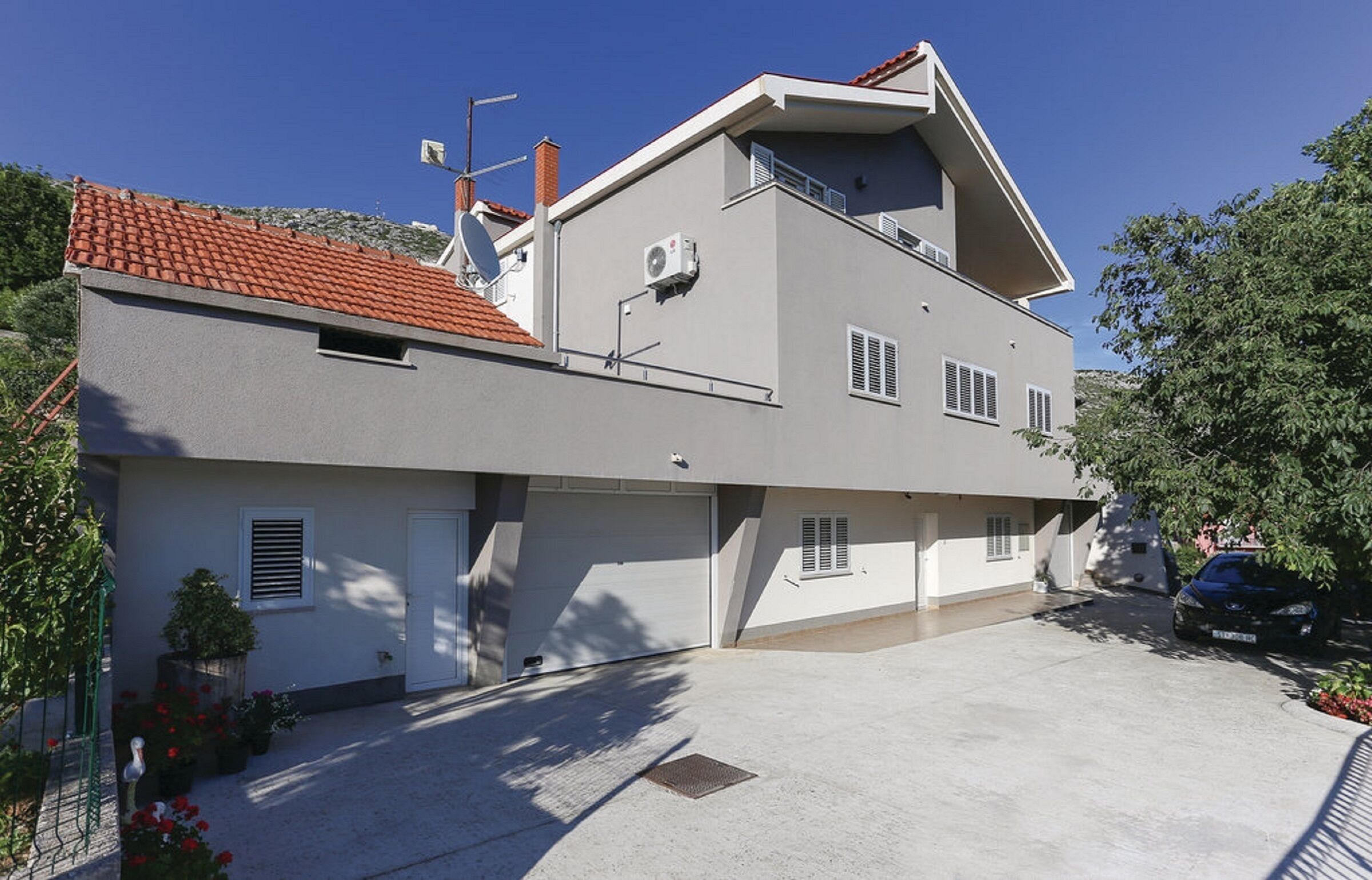 A two-story house with a red-tiled roof, a satellite dish, and a garage.