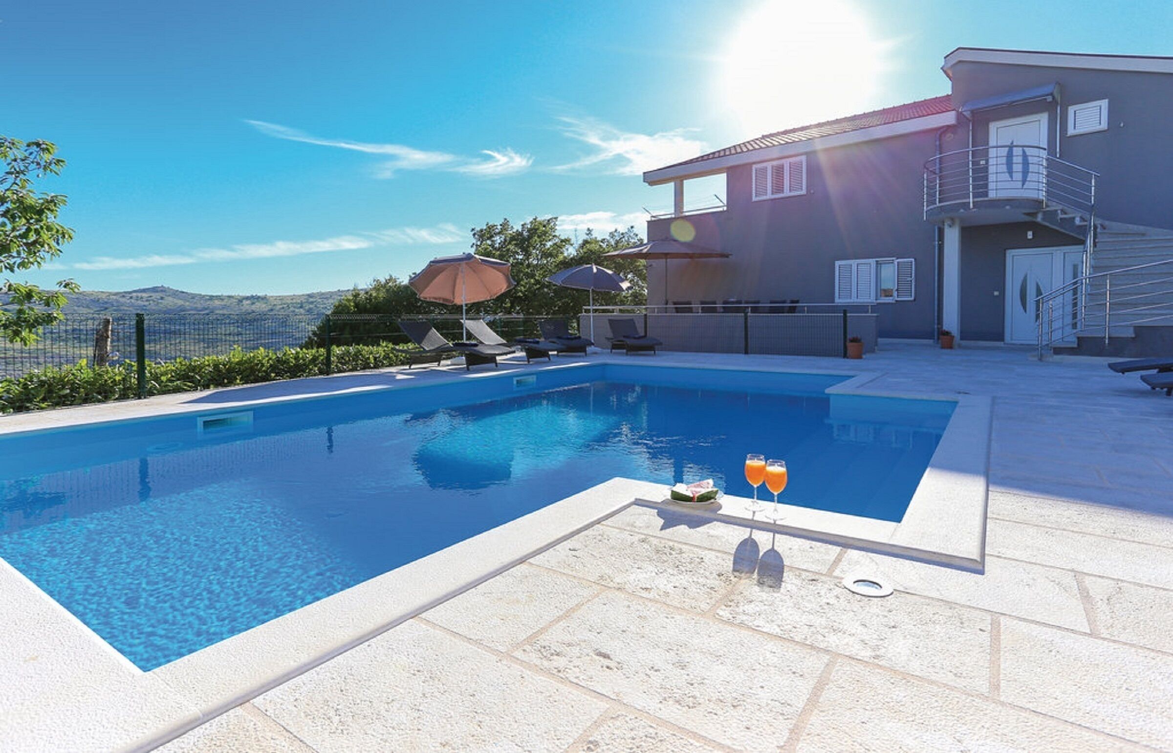 A swimming pool with lounge chairs and umbrellas, a staircase, and a view of the mountains.