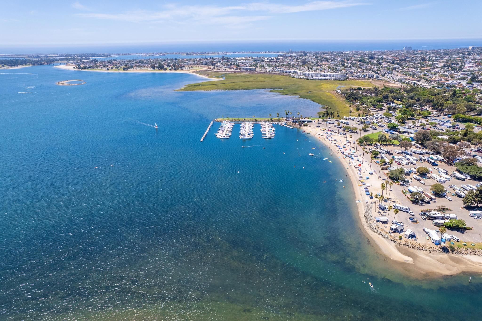Ein Luftbild einer Küstenregion mit einem Yachthafen, Strand und angrenzendem Wohngebiet.