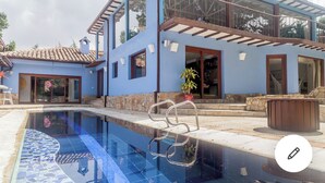 A modern two-story house with a swimming pool, large windows, and a balcony.