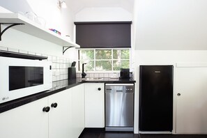 A modern kitchen with white cabinetry, a black countertop, a stainless steel dishwasher, and a black refrigerator.