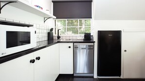 Une cuisine moderne avec des meubles blancs, un plan de travail noir, un lave-vaisselle en acier inoxydable et un réfrigérateur noir.