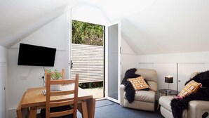 Une pièce chaleureuse avec une table et des chaises en bois, un canapé agrémenté de coussins à motifs, un téléviseur fixé au mur et une porte coulissante donnant sur un espace extérieur.