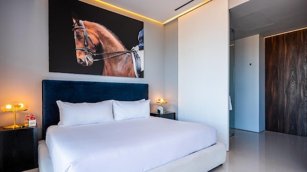 Una habitación de hotel moderna con una cama grande, un cabecero, dos mesitas de noche con lámparas y un cuadro de un caballo colgado en la pared.