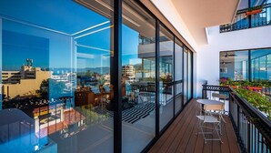 Ein moderner Balkon mit Glasgeländern, einer Holzterrasse und Gartenmöbeln.