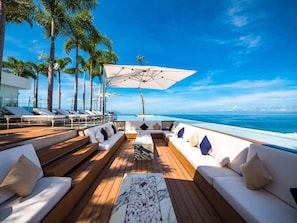 Une terrasse ensoleillée avec un plancher en bois, des canapés blancs et une table centrale.