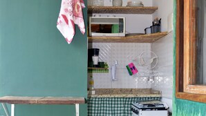 A compact kitchen with a microwave, a gas stove, and a small sink. There is a trash bin and a towel hanging on a rack.