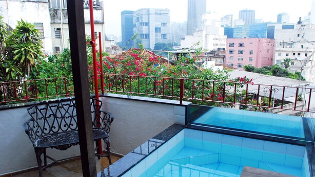 A rooftop pool with a view of the cityscape, a metal bench, and potted plants.