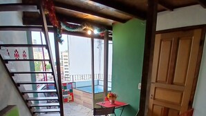 A room with a green wall, a wooden staircase, a red table with a vase, and a balcony with a pool.