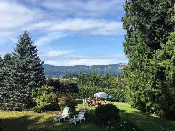 Un jardin avec deux chaises longues, une petite table et un groupe de personnes abritées sous un parasol.