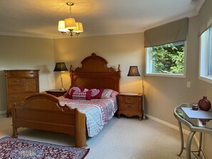 Une chambre à coucher avec un lit en bois, deux tables de chevet avec des lampes, une commode, un bureau et une fenêtre donnant sur un paysage verdoyant.