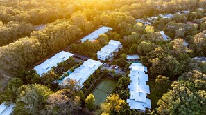 Vue aérienne d’un quartier résidentiel comprenant plusieurs maisons, un court de tennis et de nombreux arbres qui l’entourent.