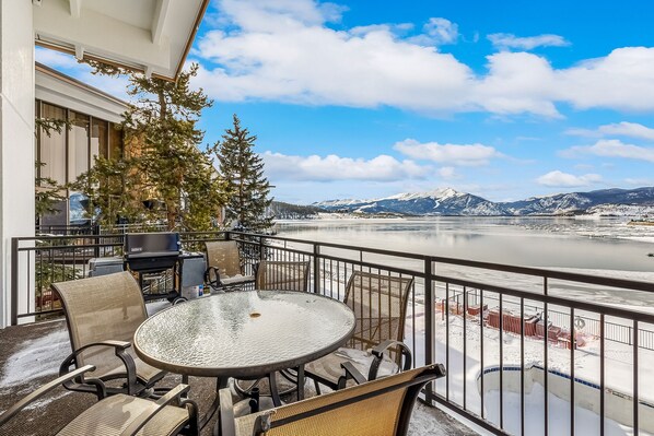 A balcony with a round table and chairs, overlooking a river and mountains.