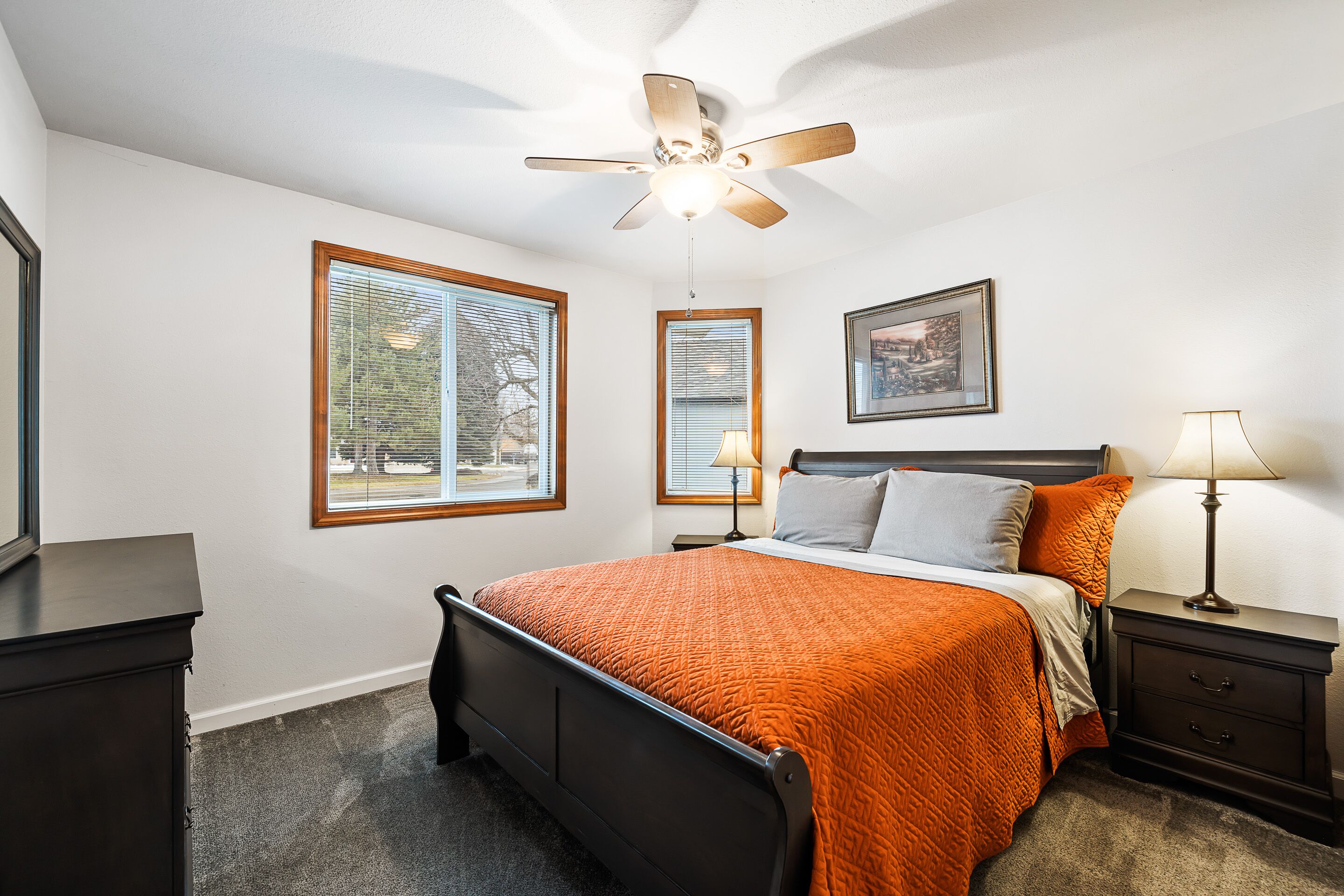 A bedroom with a bed, a ceiling fan, a nightstand, a lamp, and a framed picture on the wall.