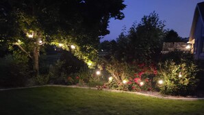 Een tuin in de schemering met lichtslingers en bloeiende planten.