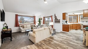 Een moderne woonkamer met een bank, salontafel en televisie. Er is een keuken met houten kastjes en een eettafel.
