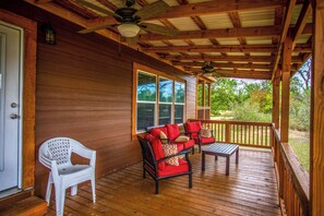 A covered porch with a wooden deck, a ceiling fan, and a seating area with a sofa and chairs. - River Bend Hideaway | 3BR Retreat w/ River Access (Medina)