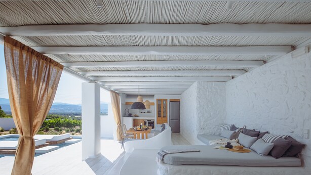 A modern, white-walled room with a built-in sofa and a view of a kitchen and outdoor area.