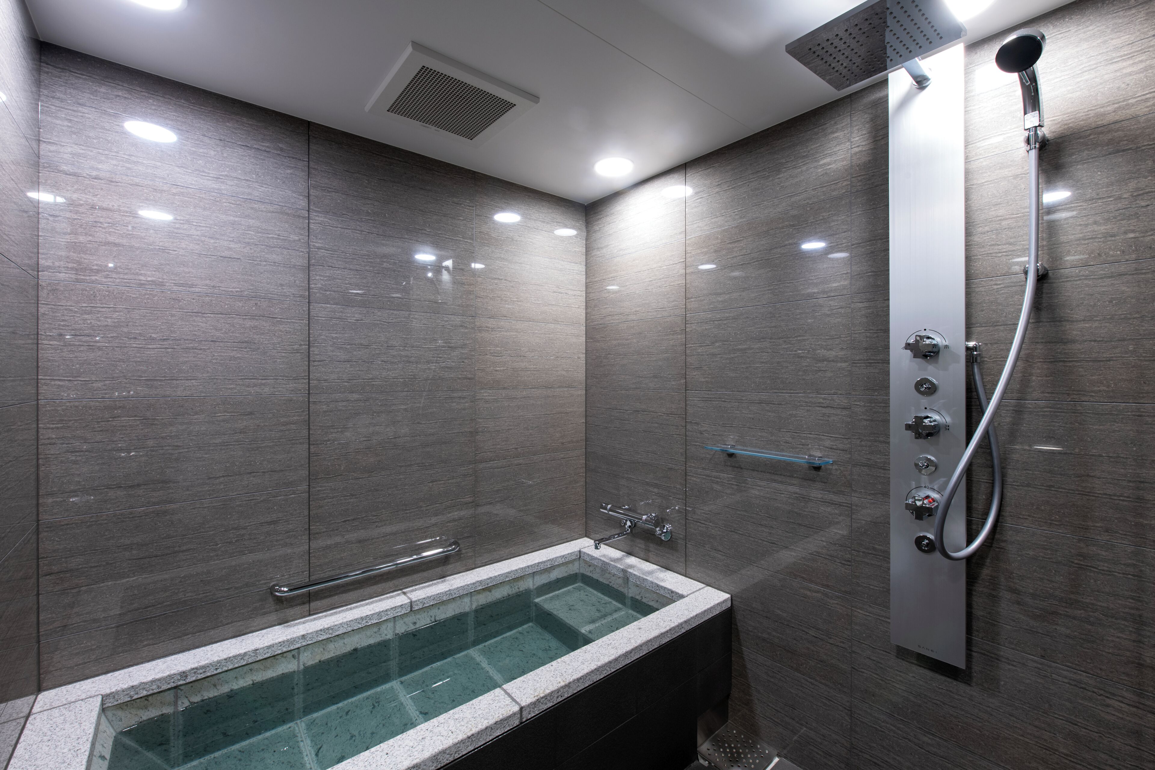 A modern bathroom with a glass-enclosed bathtub, a handheld showerhead, and a wall-mounted control panel.