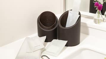 A bathroom vanity with a mirror, two brown toiletry containers, and a vase with purple flowers.