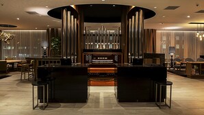 A modern hotel lobby with a central reception desk, seating area, and a decorative wall with vertical elements. - Hotel Grand Bach Sendai (Sendai)