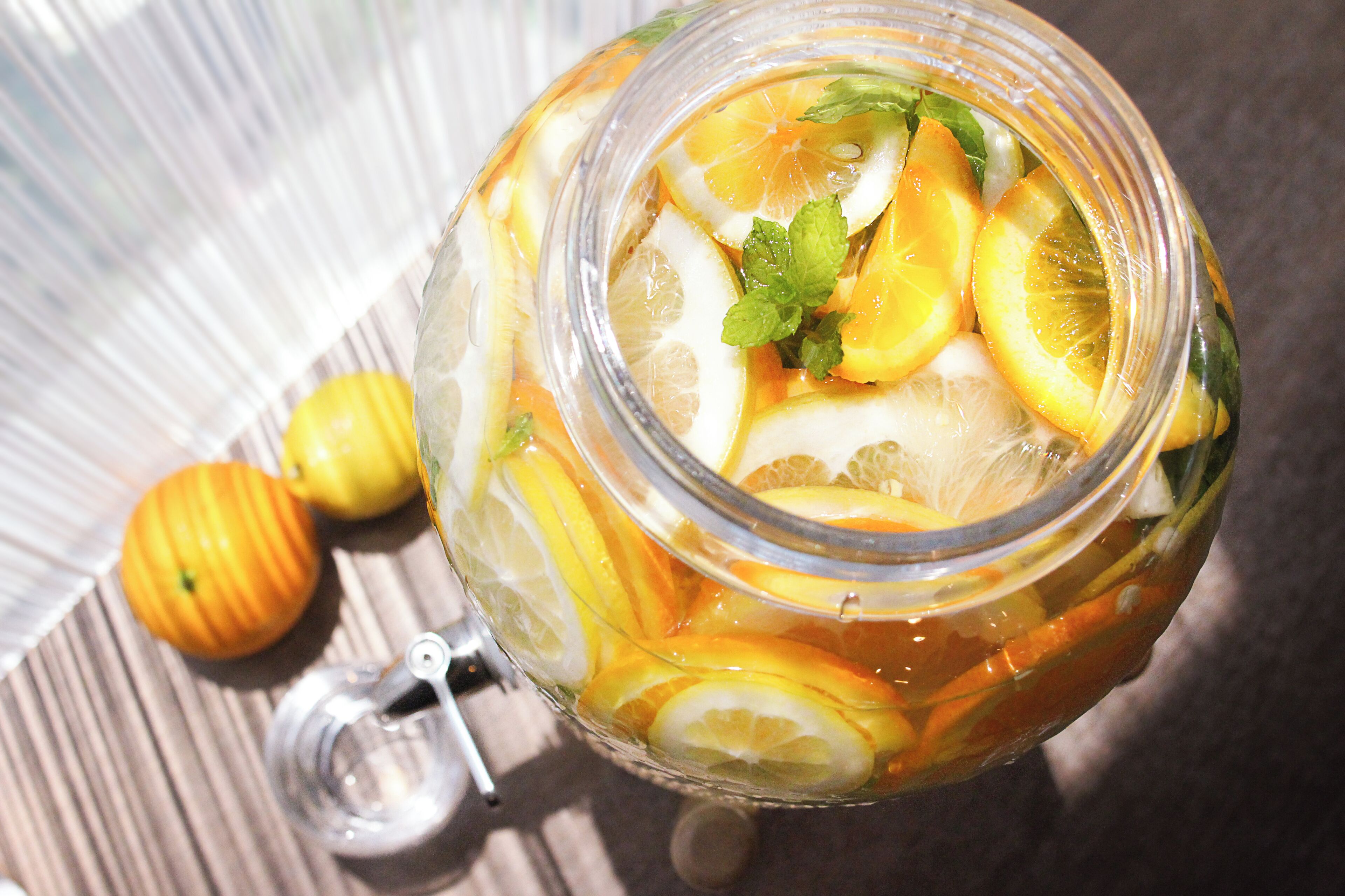 A glass jar filled with sliced oranges and lemons, with mint leaves on top.