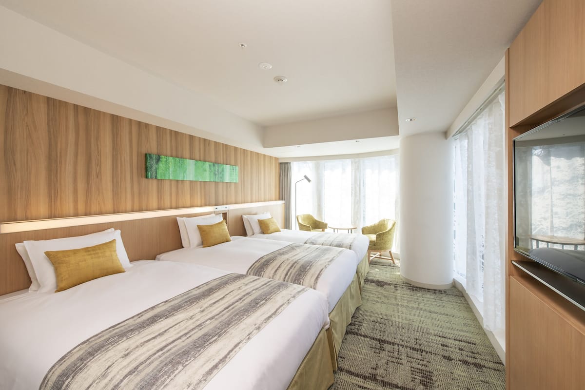 Quarto de hotel com duas camas, televisão, janela grande e vista para o exterior.