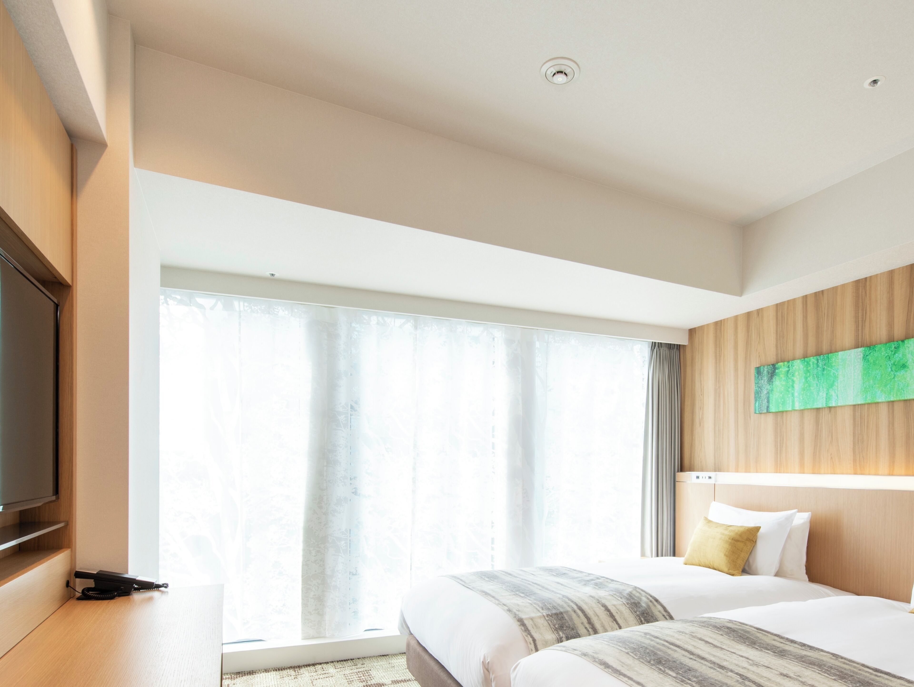 Habitación de hotel con cama, televisión de pantalla plana, ventana grande con cortinas y una pared de acento de madera.
