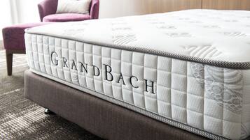 A Grandbach mattress with a quilted design, placed on a brown upholstered bench in a room with a patterned carpet.