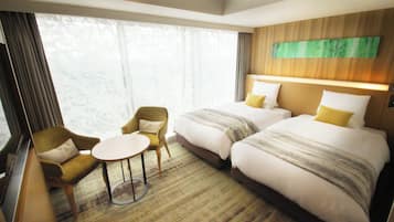 Une chambre d’hôtel avec deux lits, une télévision, une petite table, deux fauteuils et une grande fenêtre avec des rideaux.