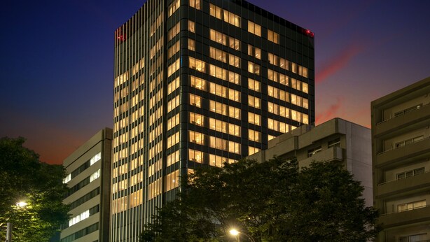 A tall hotel building with a grid of windows, a visible name sign, and surrounding trees. - Hotel Grand Bach Sendai (Sendai)