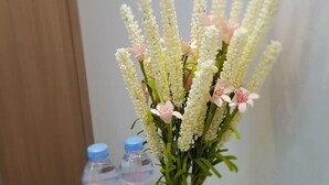 A table with a vase of flowers, two water bottles, and a red object. - Fasy Hotel (Vinh Phuc)