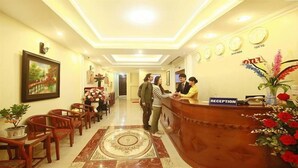A hotel reception area with a marble floor, wooden chairs, a reception desk, and a painting on the wall. - Fasy Hotel (Vinh Phuc)