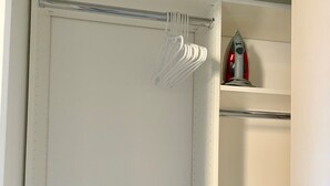 Un armario blanco con una barra para colgar y un pequeño estante con un electrodoméstico rojo.