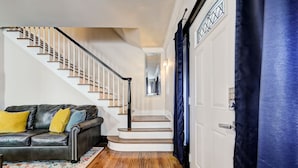 A staircase with white railings, a black leather sofa with yellow cushions, and a patterned rug.