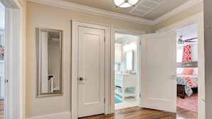 A hallway with wooden flooring, white doors, and a mirror on the left wall.