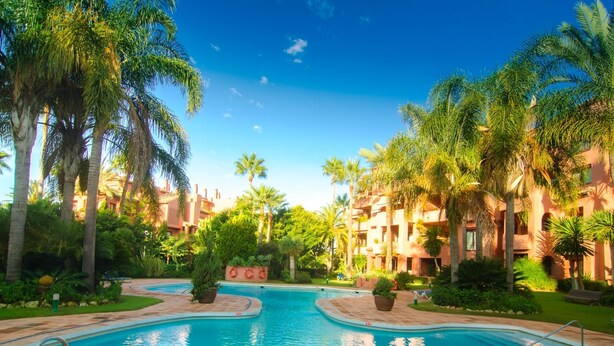 A swimming pool surrounded by palm trees and a building with balconies. - Beachfront Luxury | Renovated 2-Bed Oasis with Pool Access at Alicate Playa (Marbella)