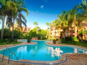 A swimming pool surrounded by palm trees and a building with balconies. - Beachfront Luxury | Renovated 2-Bed Oasis with Pool Access at Alicate Playa (Marbella)