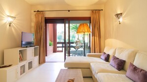 A room with a sofa, a television on a cabinet, and a view of the outdoors through a glass door. - Beachfront Luxury | Renovated 2-Bed Oasis with Pool Access at Alicate Playa (Marbella)