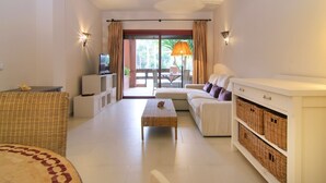 A modern living room with a sofa, a television, a coffee table, and wicker furniture. - Beachfront Luxury | Renovated 2-Bed Oasis with Pool Access at Alicate Playa (Marbella)