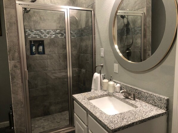A bathroom with a glass-enclosed shower, a granite countertop sink, and a large mirror. - Cozy, Pet friendly 1- bedroom cottage (San Antonio)