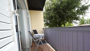A balcony with a chair and a table, a sliding glass door, and a tree in the background. - Apartment Sunny on the first floor (Njivice)