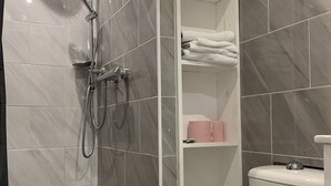 A bathroom with a shower, toilet, and shelves with towels. - Magnificent Studio in the historic heart of Fréjus (Fréjus)