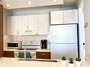 A modern kitchen with white cabinets, a stainless steel refrigerator, a microwave, an oven, and a coffee maker.