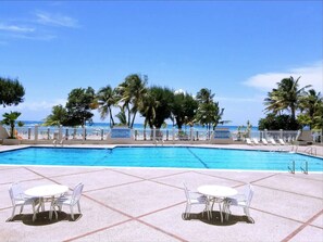A pool area with clear blue water, surrounded by palm trees and a view of the ocean.