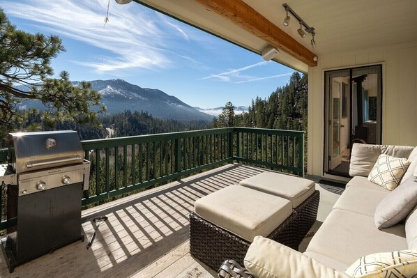 A balcony with a grill, wicker furniture, and a view of mountains.